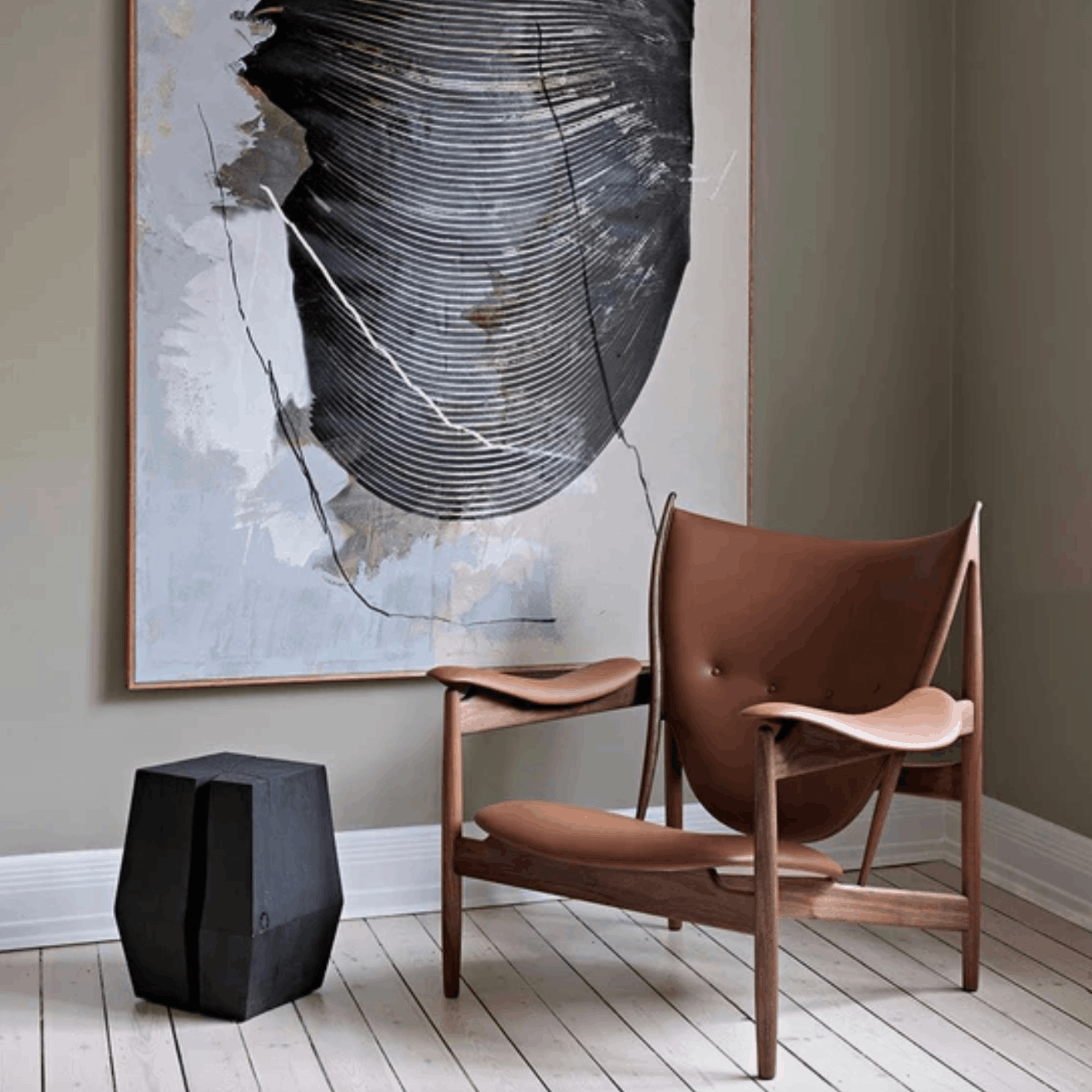 Modern brown leather chair in a room with abstract art and a black cube.