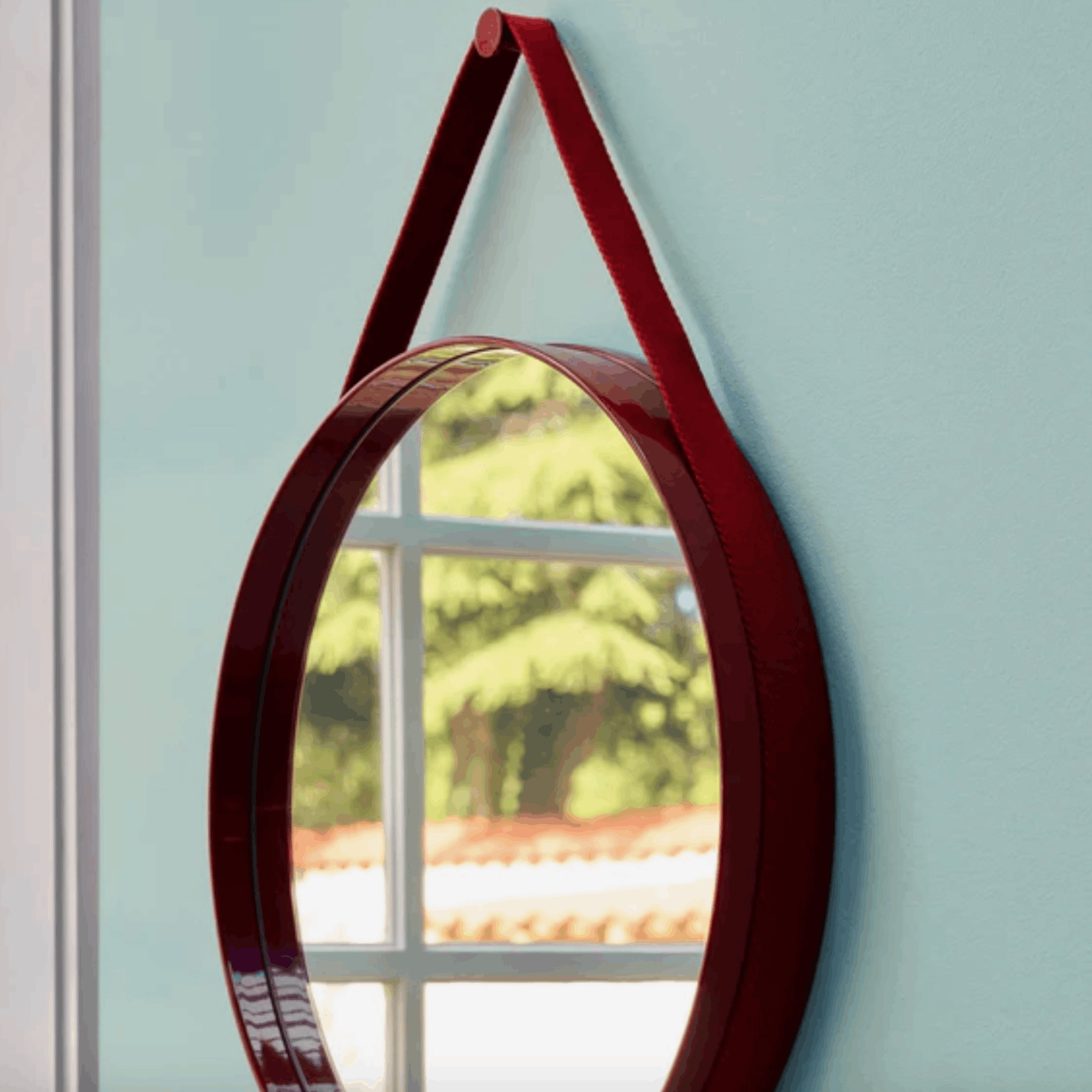 A contemporary round wall mirror by HAY featuring a minimalist steel strap design, perfect for bedrooms, bathrooms, and hallways.