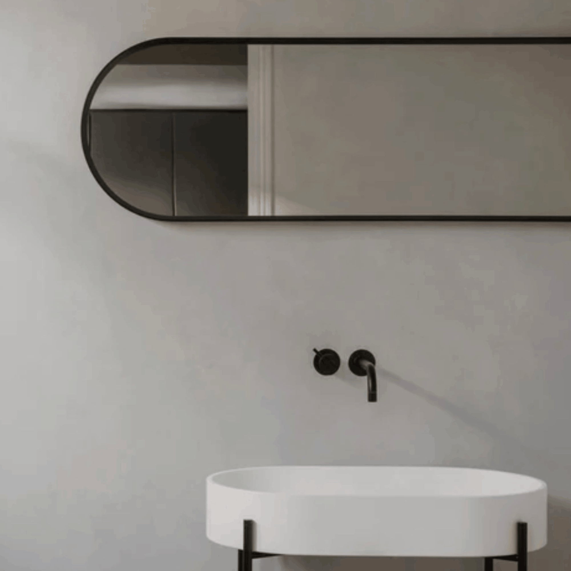 The Audo Copenhagen Norm Mirror hanging on a grey wall above a white marble sink with black taps in a modern bathroom