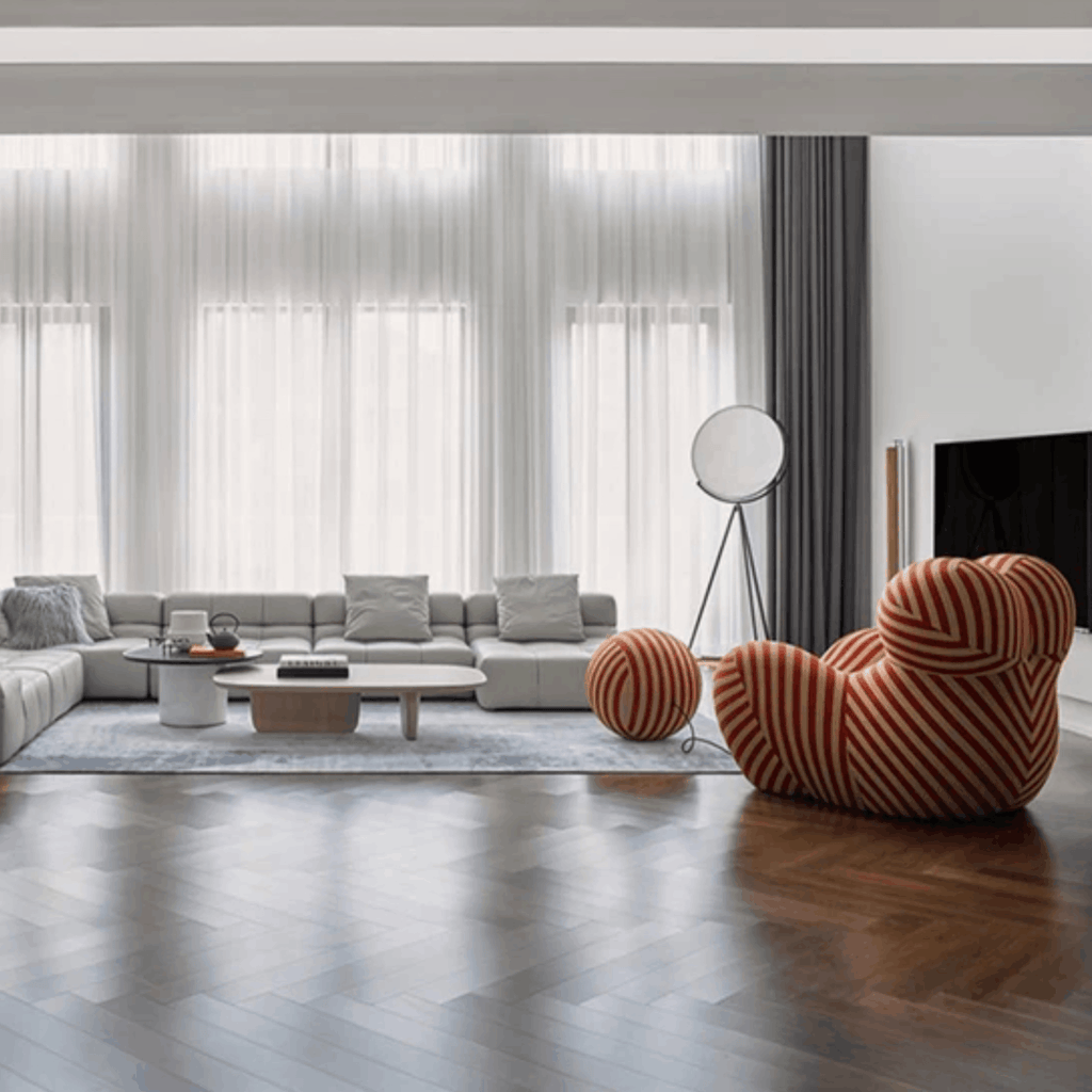 Modern living room with a gray sectional sofa, striped armchair, and large windows.