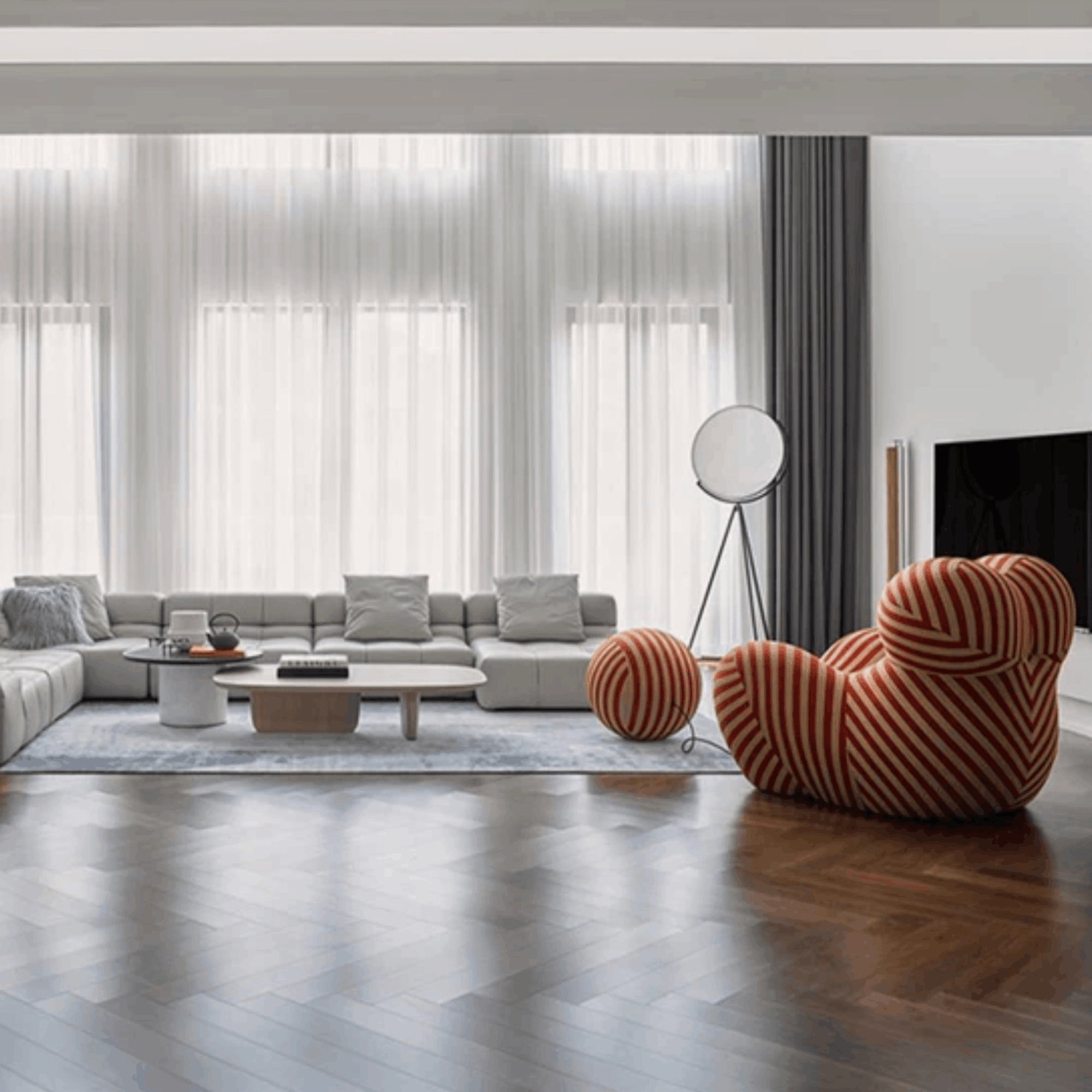 Modern living room with a gray sectional sofa, striped armchair, and large windows.