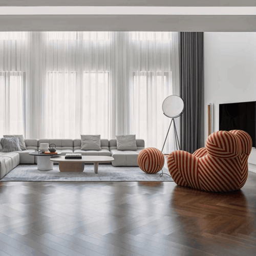 Modern living room with a gray sectional sofa, striped armchair, and large windows.