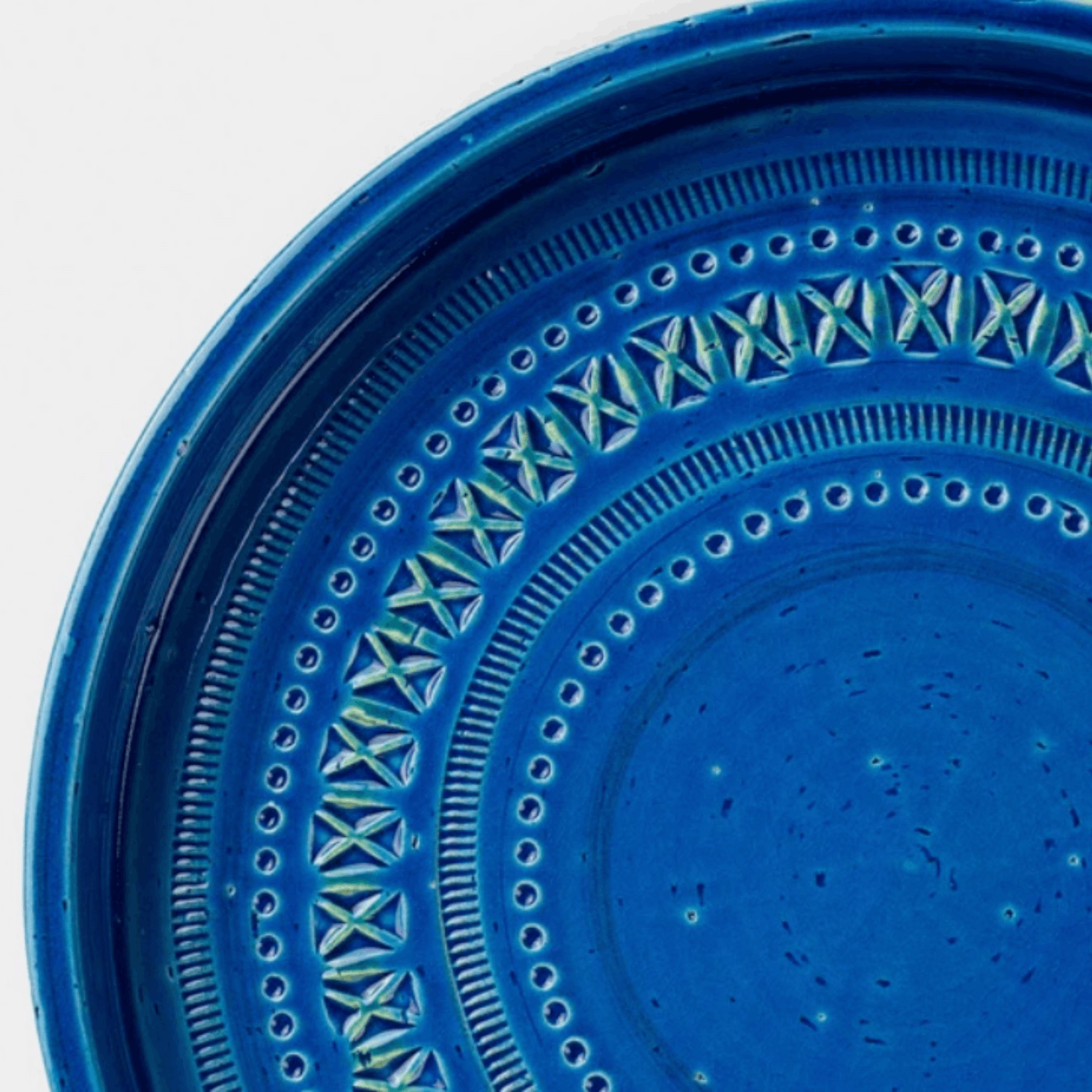 A close-up of a vibrant cobalt blue ceramic plate with concentric circular patterns and textured geometric details.