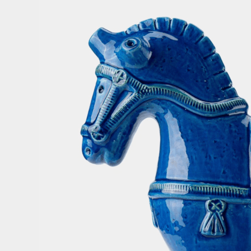 A close-up of a glossy blue ceramic horse figurine, showing its head and neck with decorative bridle details, set against a plain light gray background.