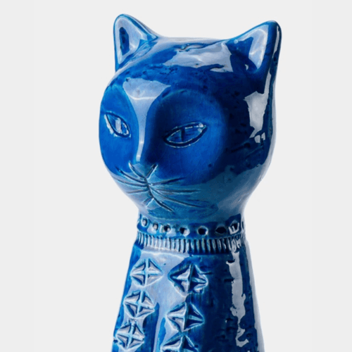 A glossy blue ceramic cat figurine with carved facial features and geometric patterns on its body, shown against a plain light gray background.