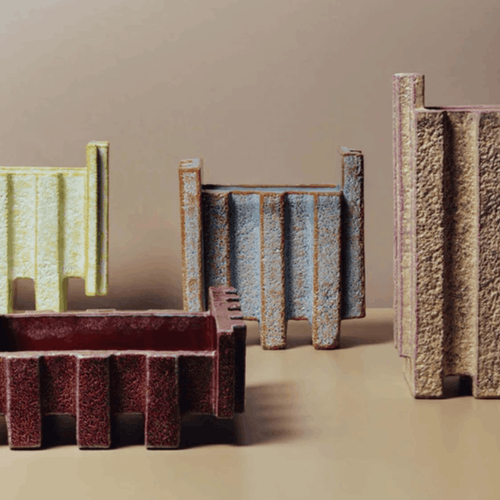 A set of textured vases in various colors including dark red-brown, light blue, beige, and pale yellow, arranged on a neutral beige background.