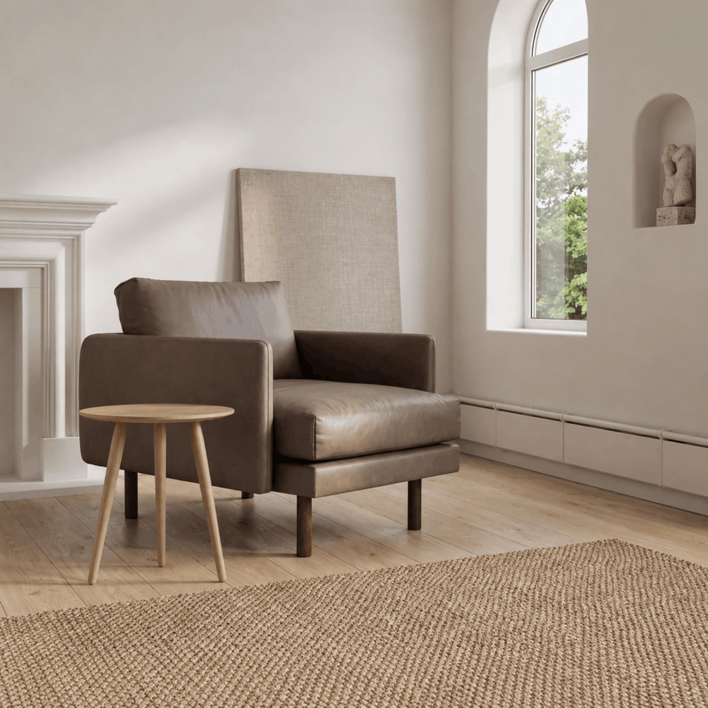 Bruunmunch PLAYround round coffee table in white oiled oak in a modern living room in front of a walnut coloured leather arm chair on an oak floor with white walls