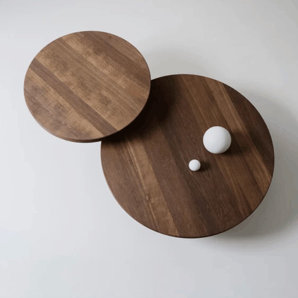 Two round wooden coffee tables in dark brown walnut wood grain, with one table partially slid off the other, styled with two small white spherical objects on a light gray background.