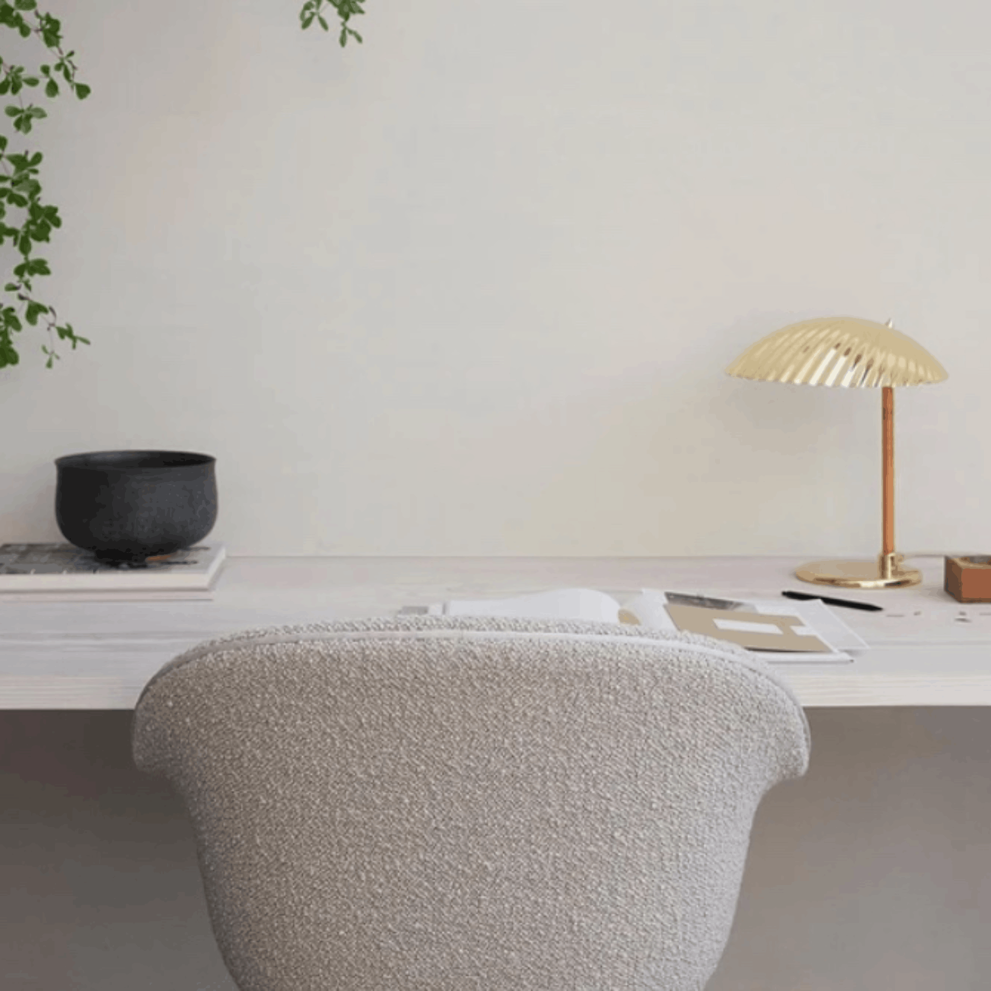 A modern textured light gray boucle office chair in a minimalist home office setting next to a gold pleated table lamp on a white desk.
