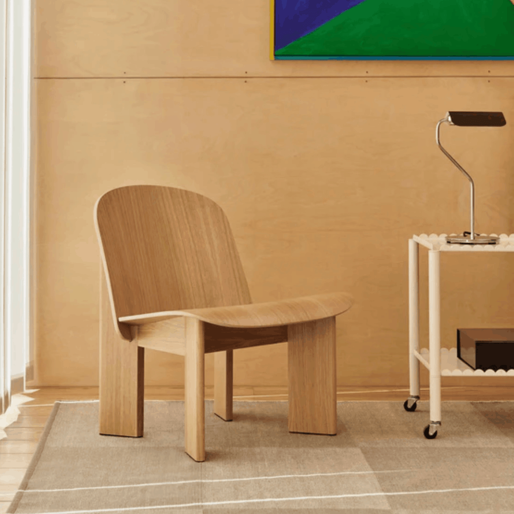 Wooden chair in a room with a beige wall and a small table with a lamp.