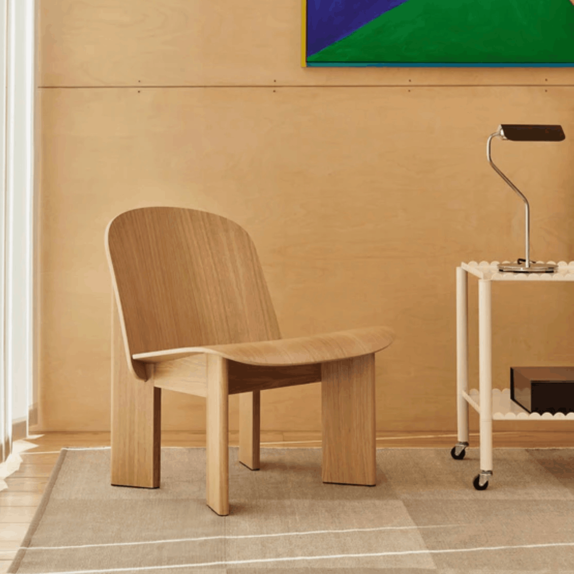 Wooden chair in a room with a beige wall and a small table with a lamp.