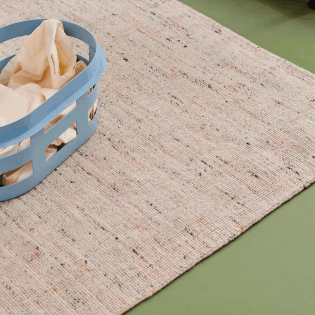Textured beige rug with a blue laundry basket on a green floor.