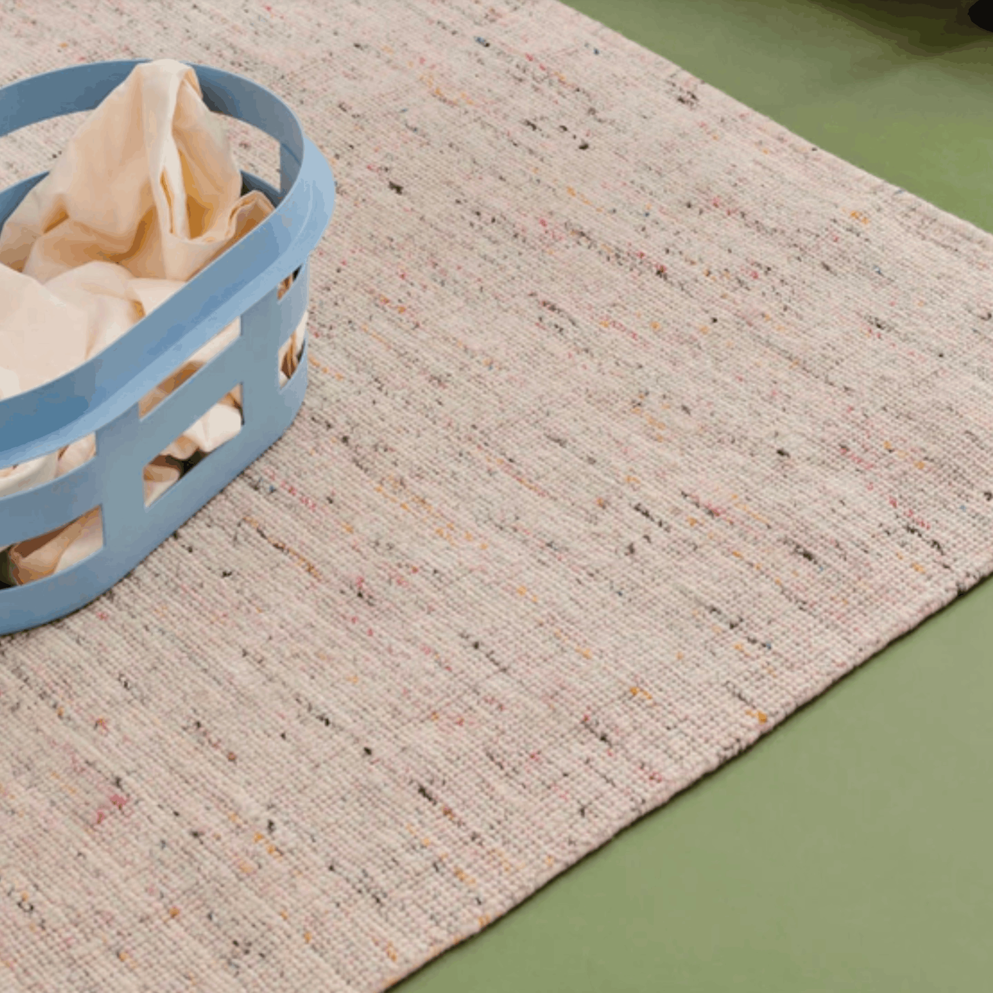 Textured beige rug with a blue laundry basket on a green floor.