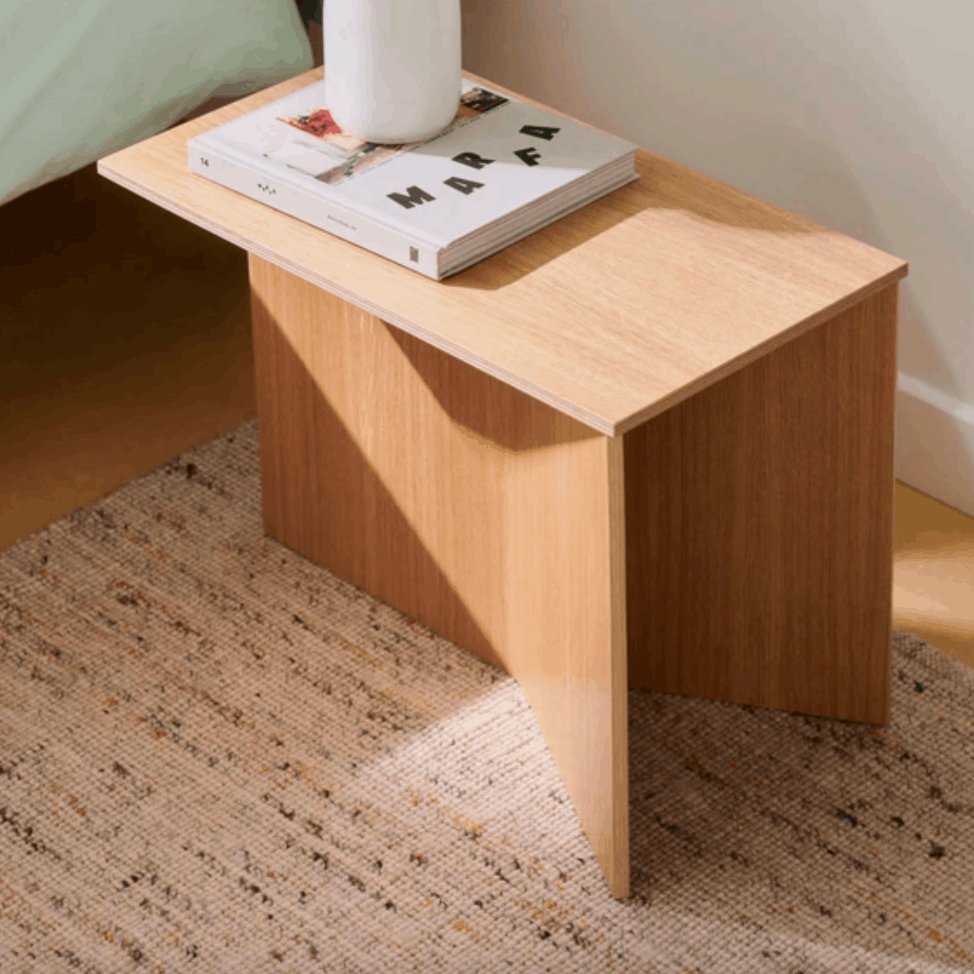 Wooden side table with a book and a white vase on a Hays Crayon effect rug.