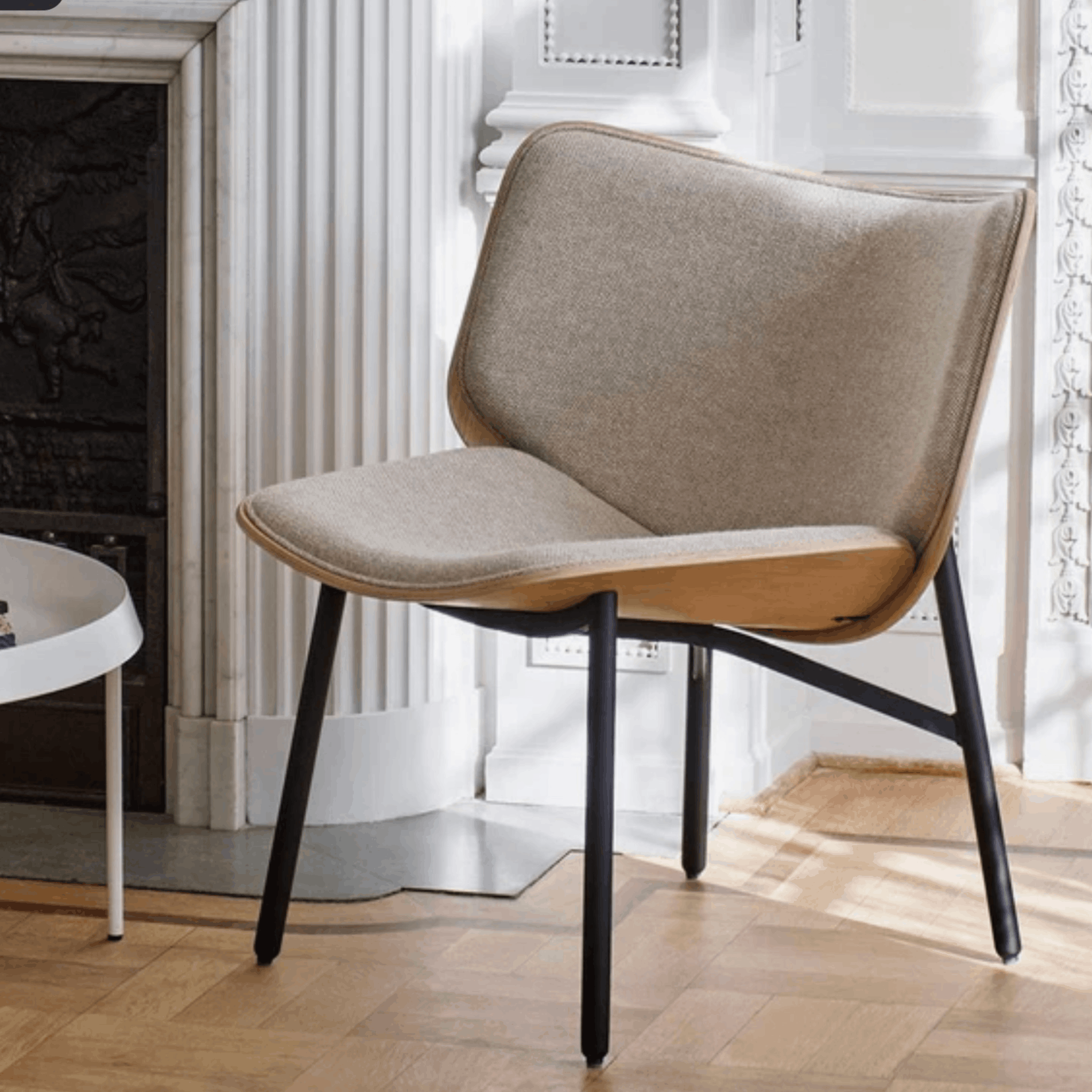 Modern chair with wooden seat and black metal legs in a room with white walls and a fireplace.