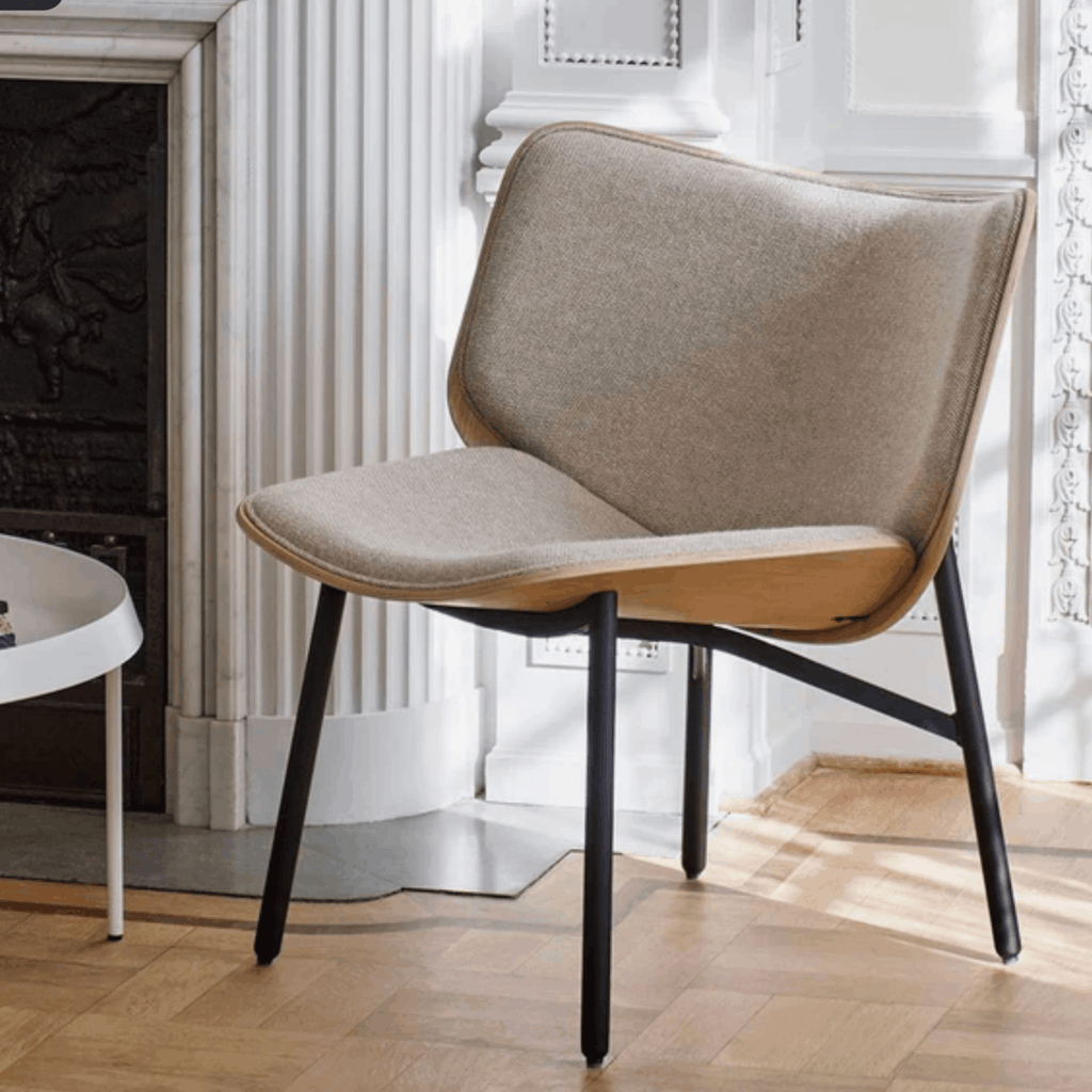 Modern chair with wooden seat and black metal legs in a room with white walls and a fireplace.