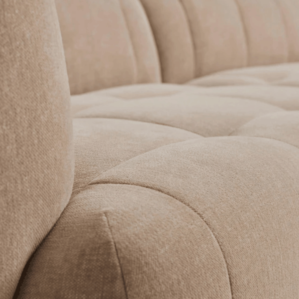 Close-up of a beige tufted upholstered sofa showing the fabric texture and padded armrests.