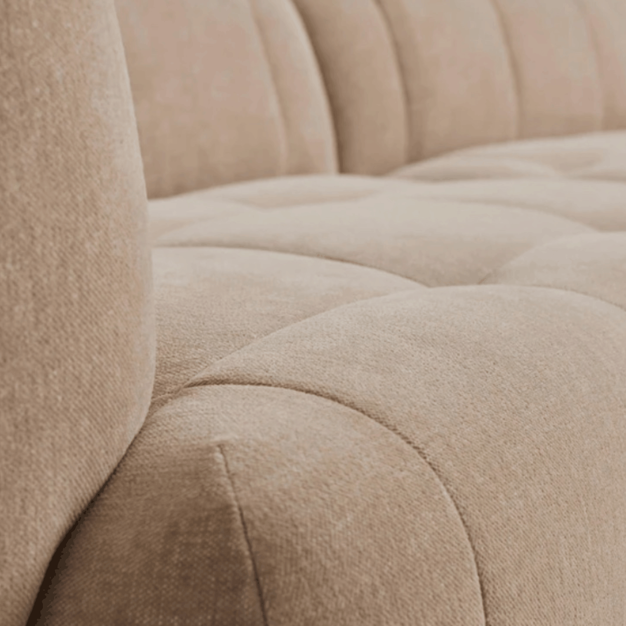 Close-up of a beige tufted upholstered sofa showing the fabric texture and padded armrests.