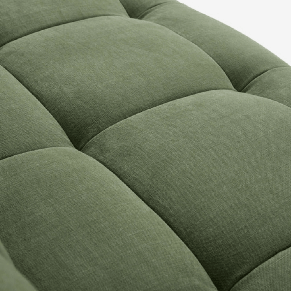 Close-up of a tufted upholstered sofa in a muted sage green fabric, showing the texture and padded segmented design.