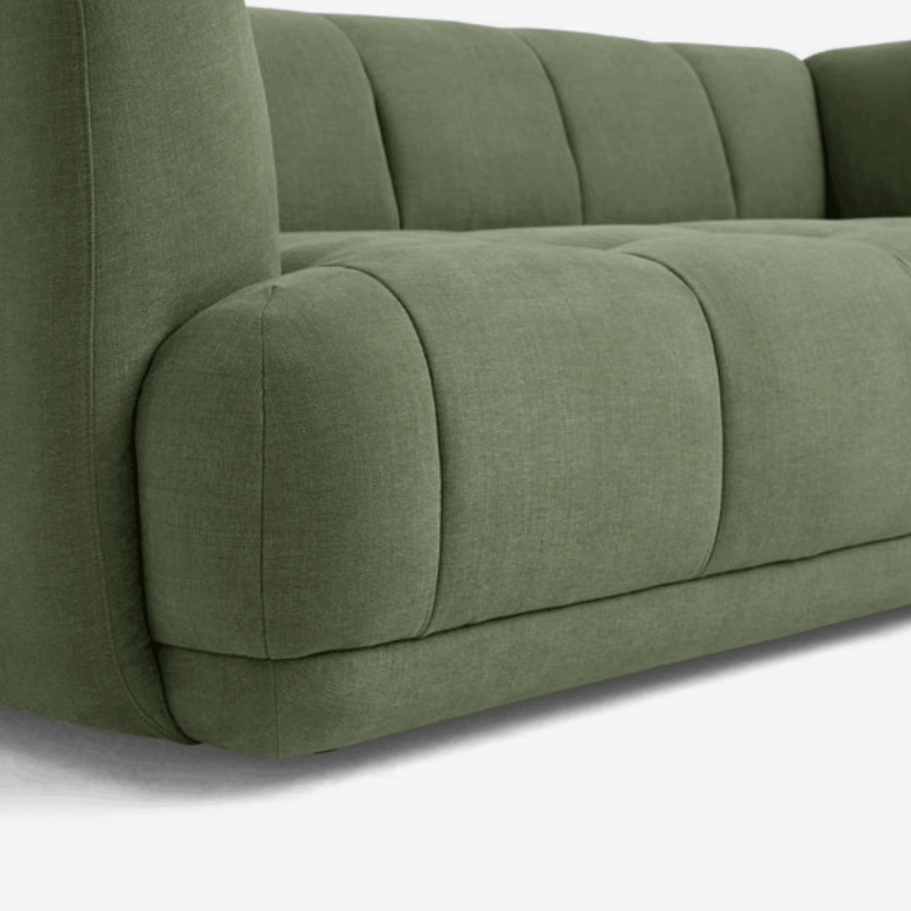 Close-up of a modern upholstered sofa in a muted sage green fabric, showing the tufted backrest and armrest details against a clean white background.