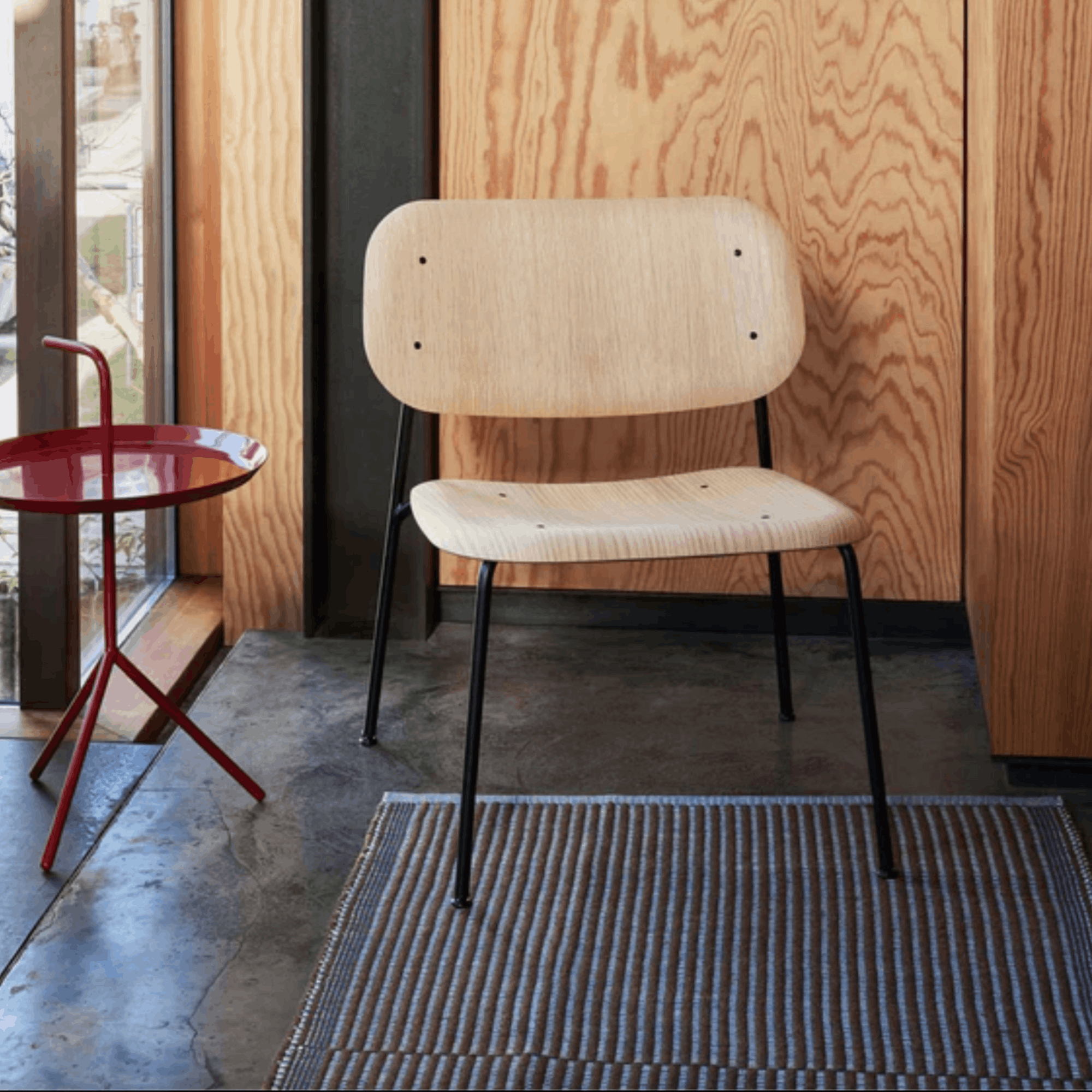 Beige chair with black legs in a room with wooden walls, a red side table and a Hays Chestnut and Blue rug on the floor.