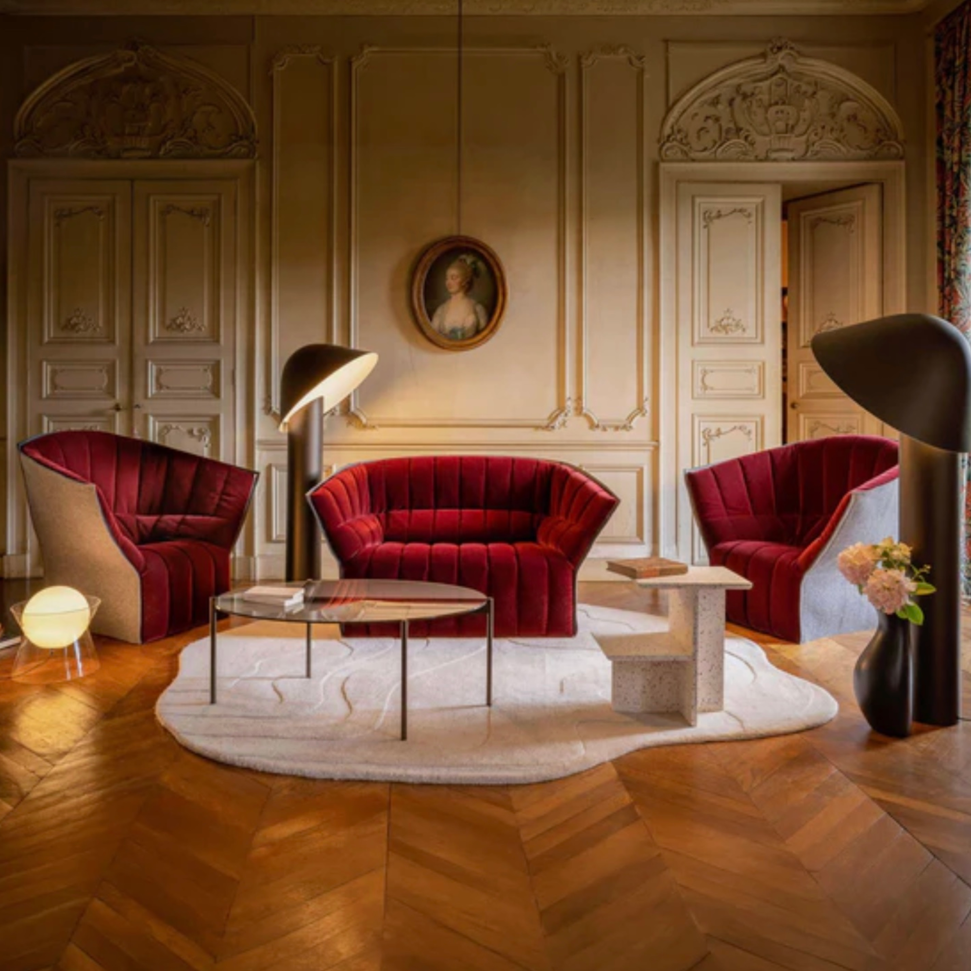 Luxurious living room with red velvet sofa and armchairs, marble coffee table, and decorative elements such at a large Ligne Roset Gavrinis rug