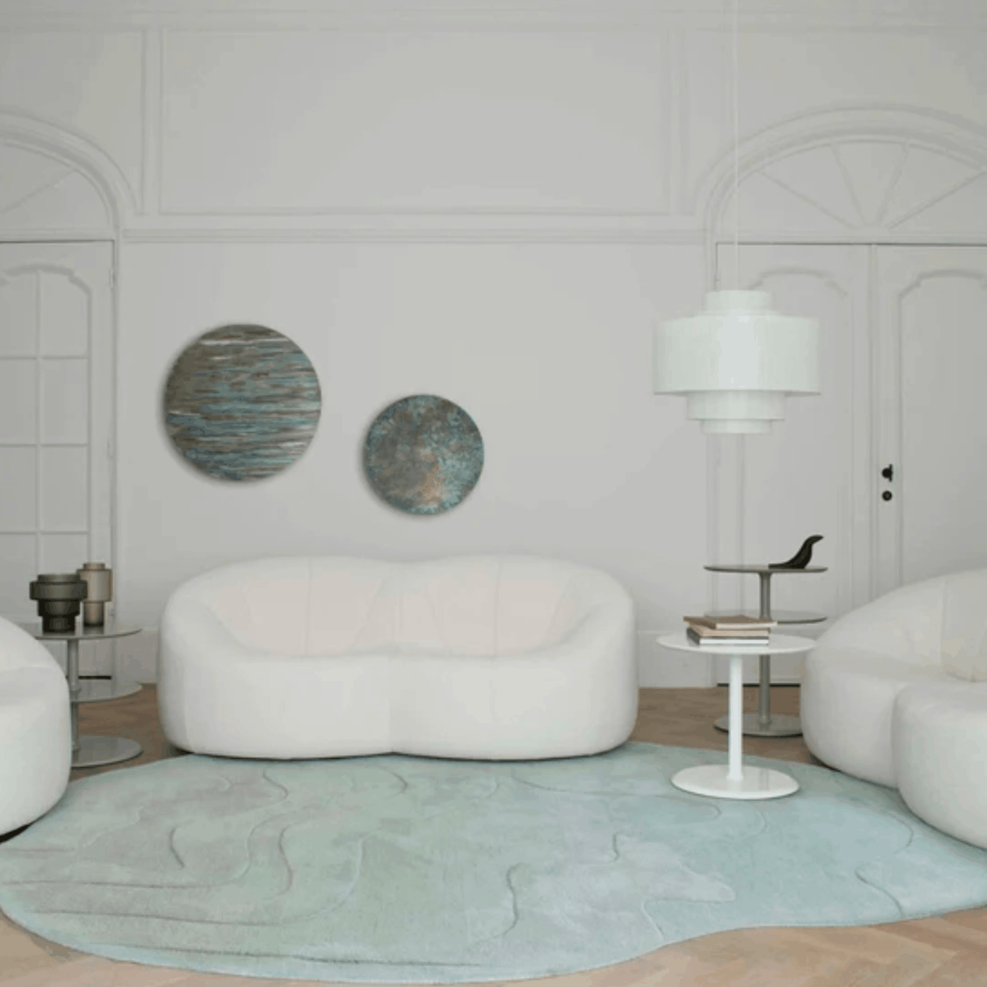 Modern living room with white furniture, a light blue Ligne Roset Gavrinis rug, and decorative wall art.