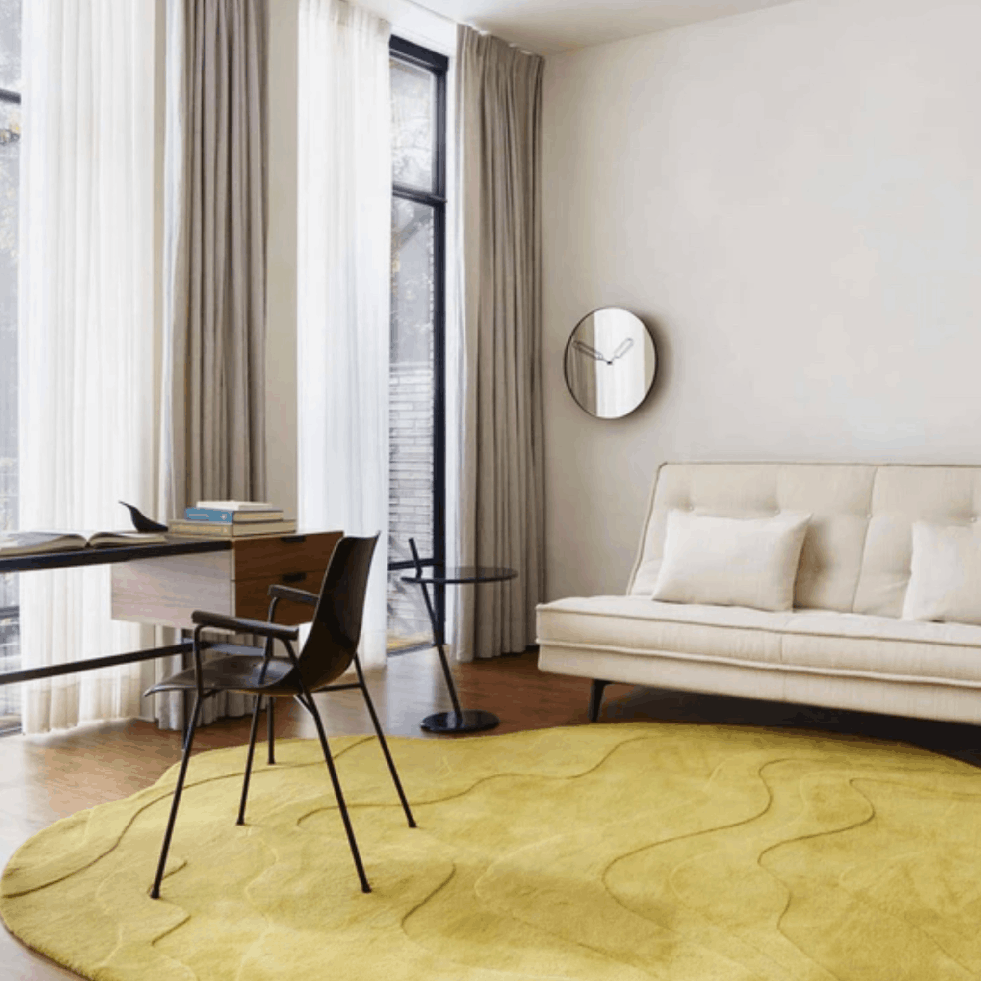 Modern living room with a mustard Ligne Roset Gavrinis rug, beige sofa, and glass desk.