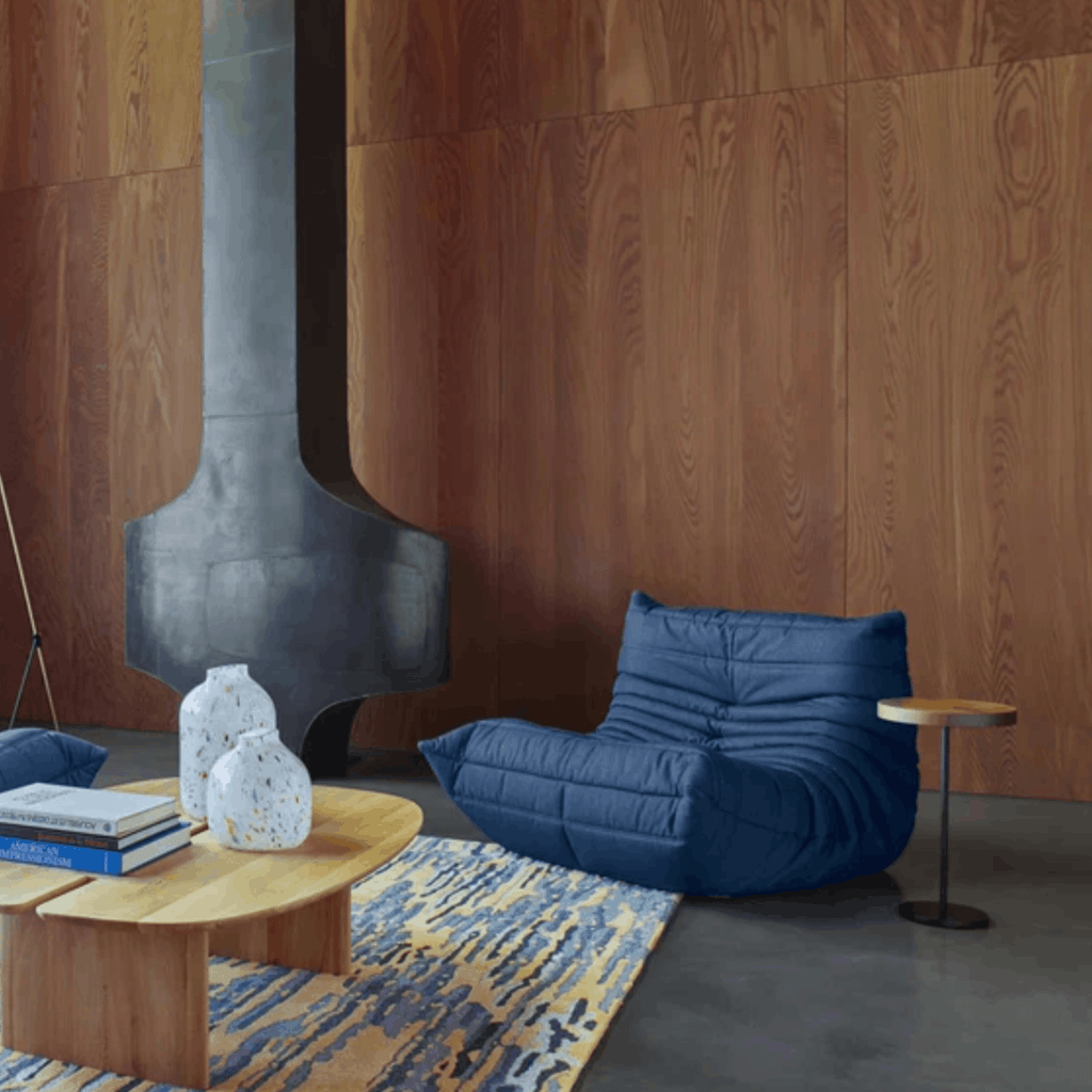 Modern living room with a blue bean bag chair, wooden coffee table, and abstract art on a wooden wall.