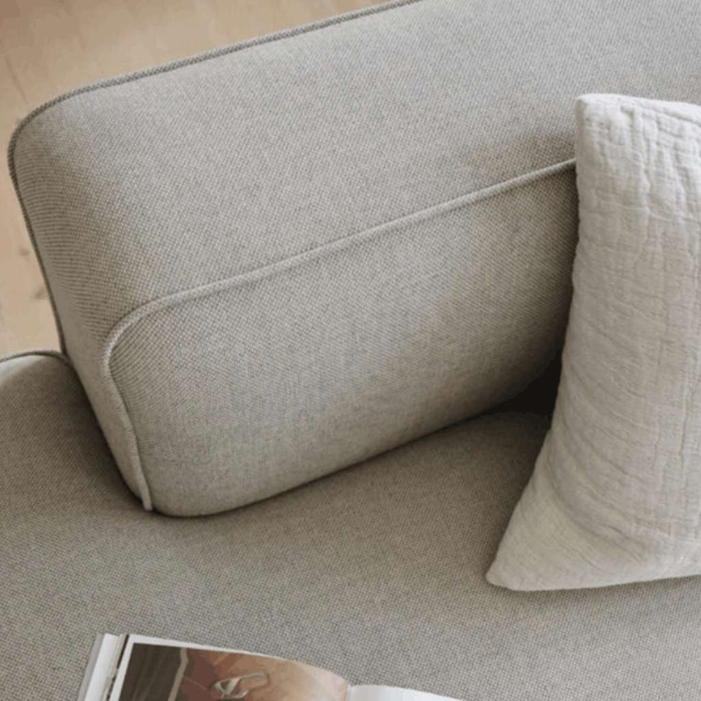 Close-up of a light beige upholstered sofa with a matching textured throw pillow and part of an open magazine visible in the foreground.