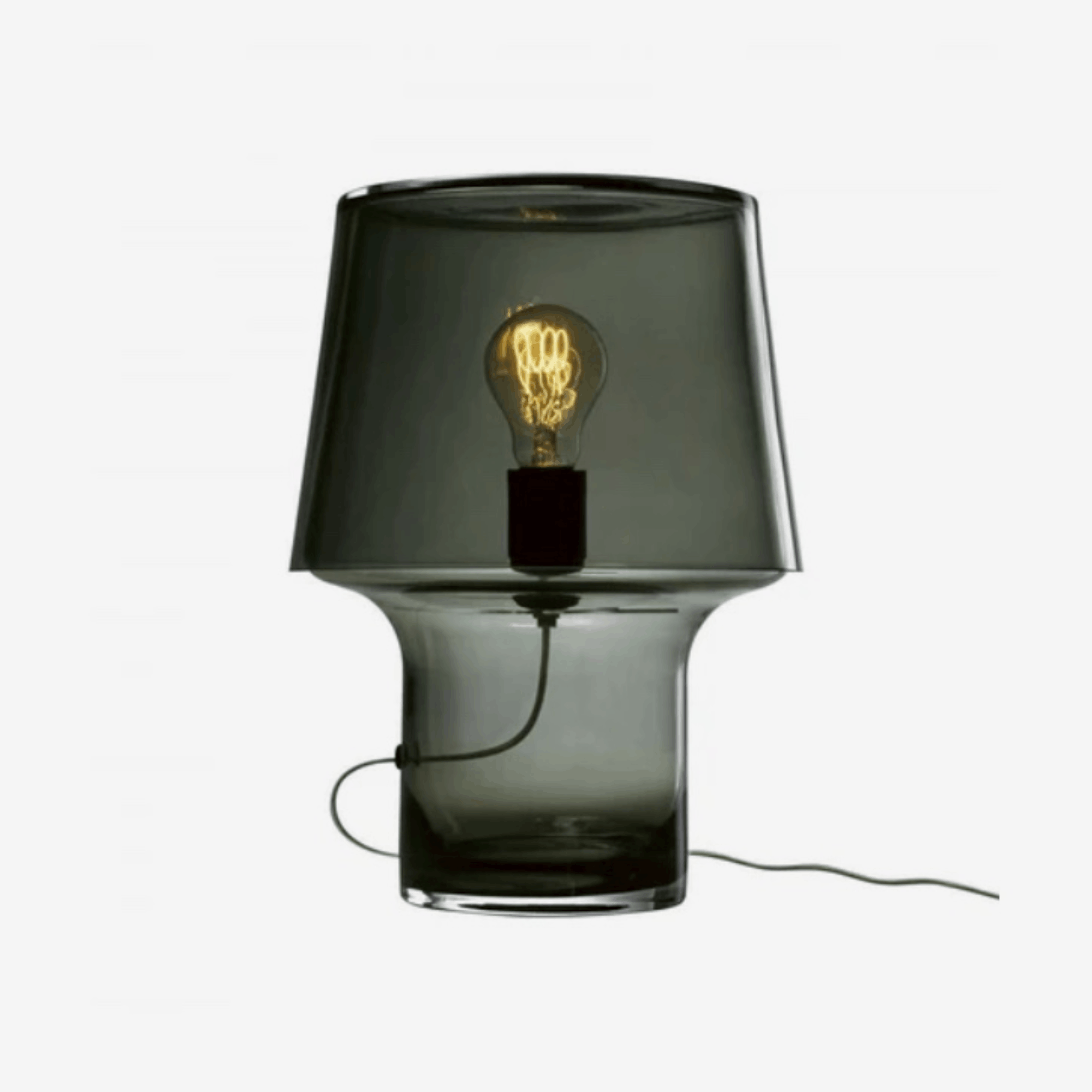 The Muuto Cosy Table Lamp by Harri Koskinen features a sculptural mushroom-shaped design crafted from smoked grey mouth-blown glass. With soft diffused light and mains dimming compatibility, it brings warm Scandinavian style and ambient lighting to contemporary interiors.