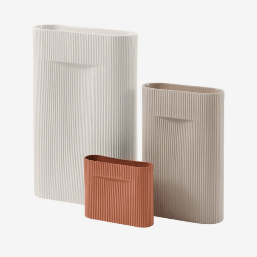 Three ribbed ceramic vases in off-white, beige, and terracotta, arranged on a light gray background.