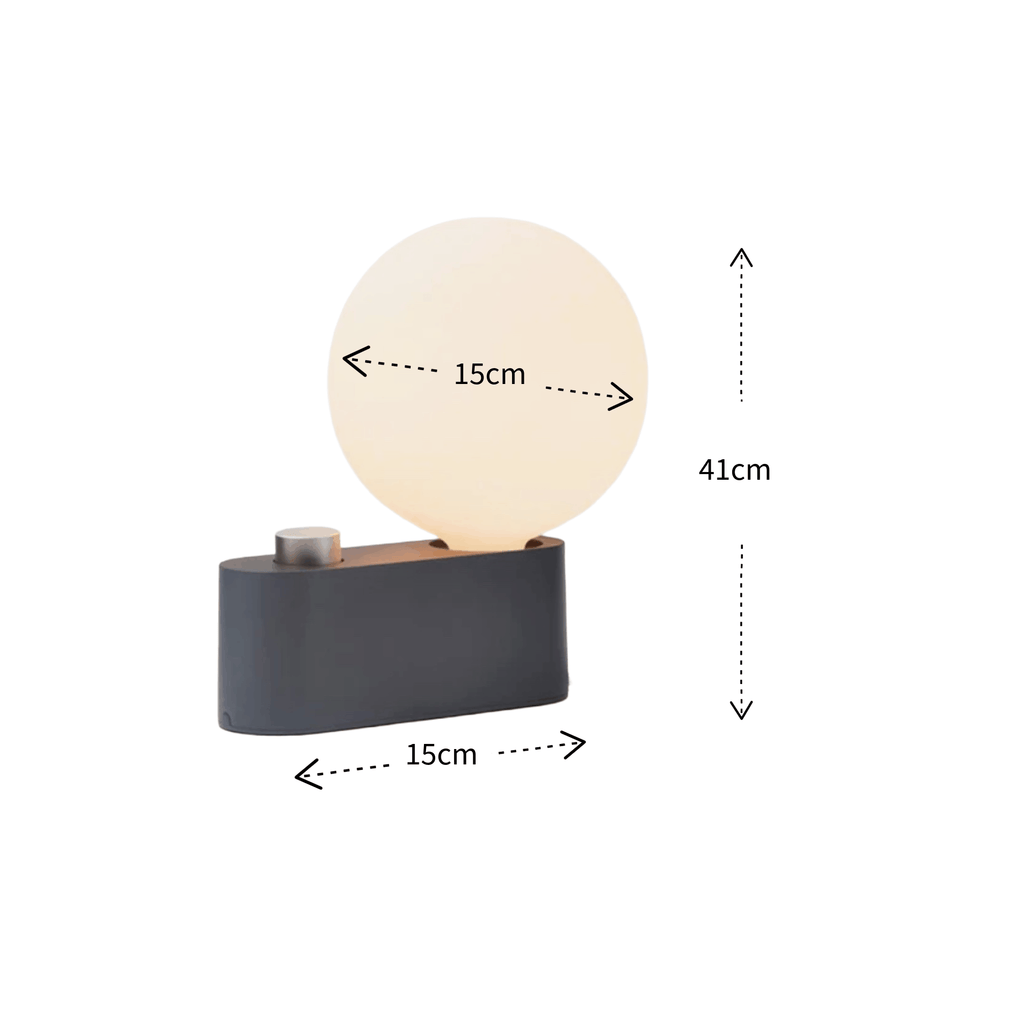 A modern table lamp with a matte black rectangular base, a small metallic button, and a glowing warm white spherical shade. Dimension arrows and labels indicate a height of 41cm, width of 15cm, and depth of 15cm on a plain white background.