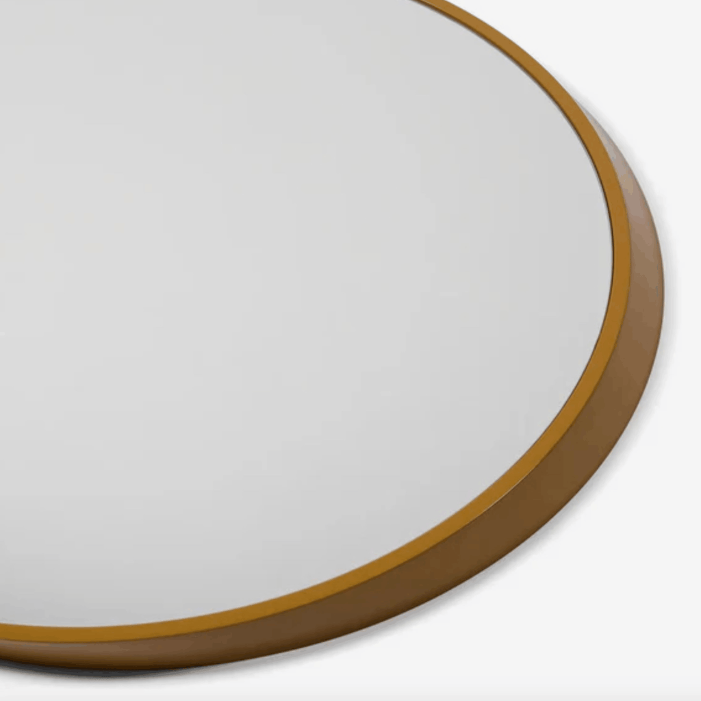Close-up of a round wall mirror with a warm brown wooden frame, showing a portion of the reflective glass surface against a light gray background.