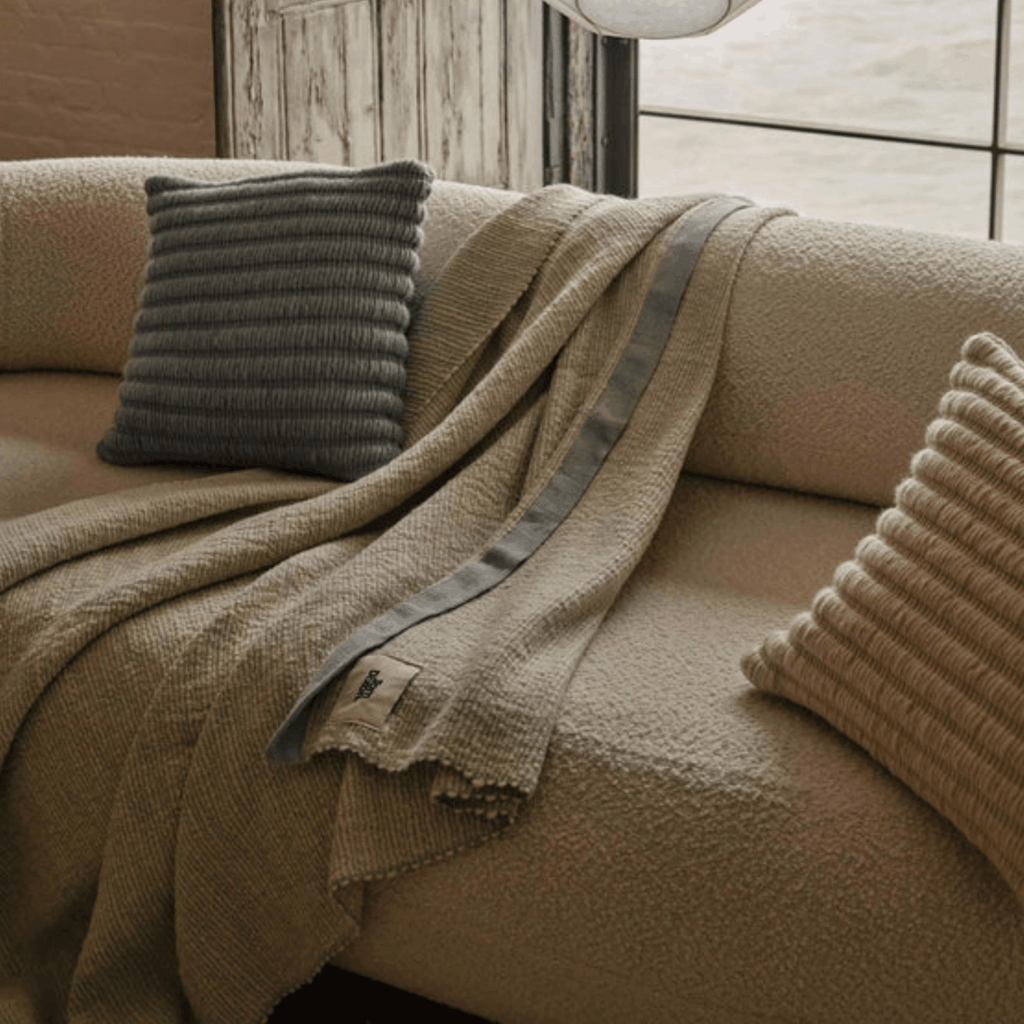 Beige sofa with a textured blanket and Tom Dixon pillows in a cozy room.