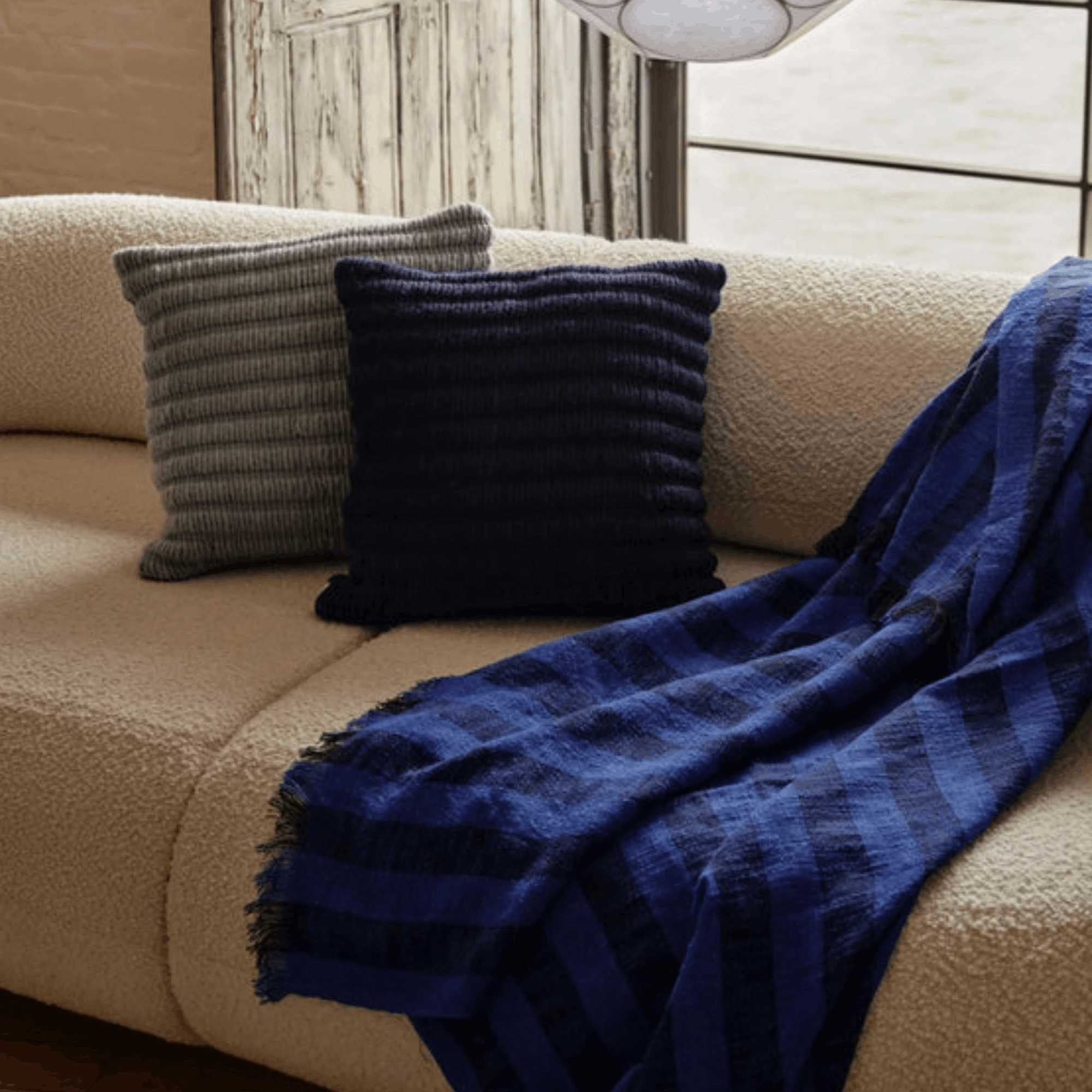 Beige sofa with blue plaid throw and dark blue pillow in a cozy living room setting.