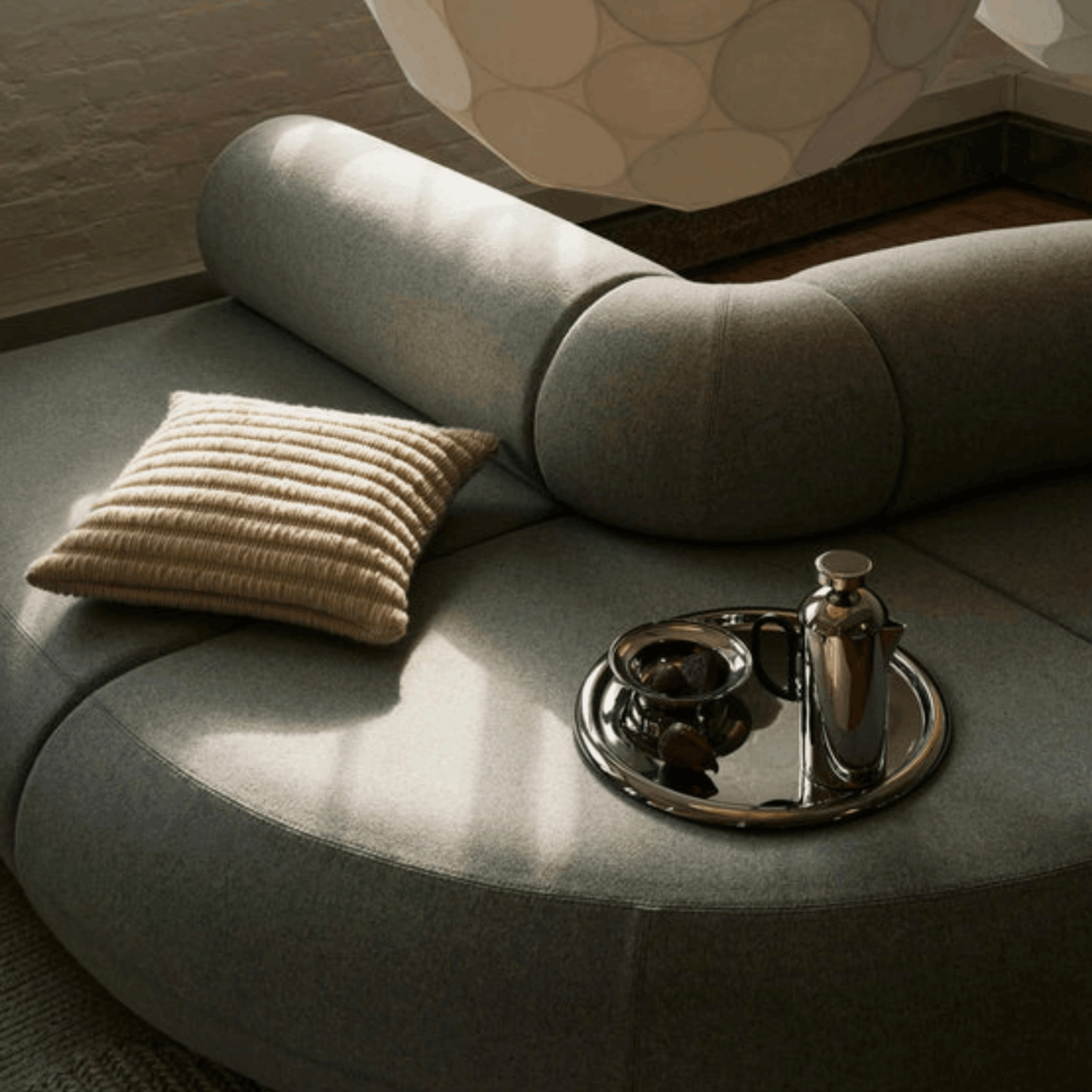 Round gray sofa with a textured pillow and decorative items on a tray