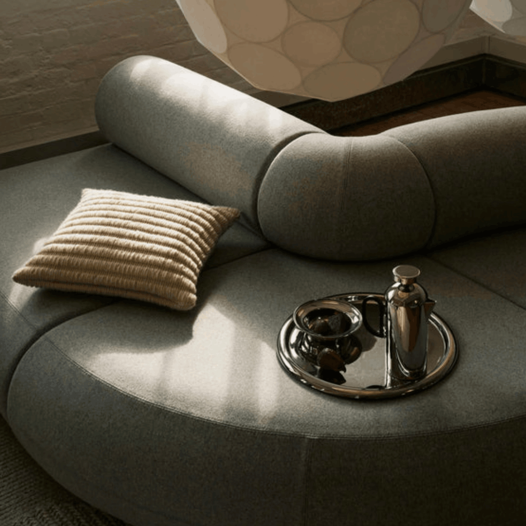 Round gray sofa with a textured pillow and decorative items on a tray