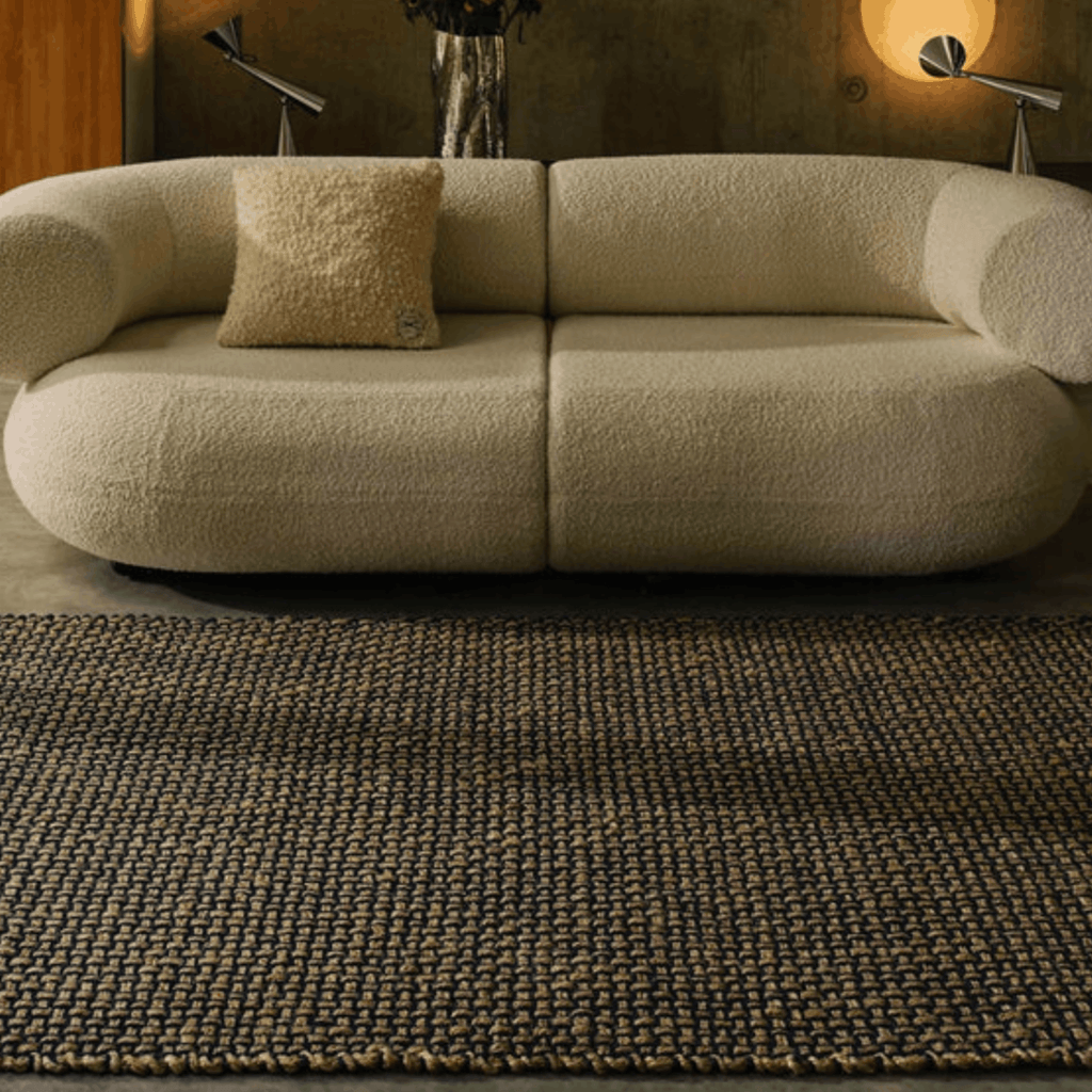 A cream bouclé sofa with a matching throw pillow in a styled living room, positioned on top of a Tome Dixon woven rug.