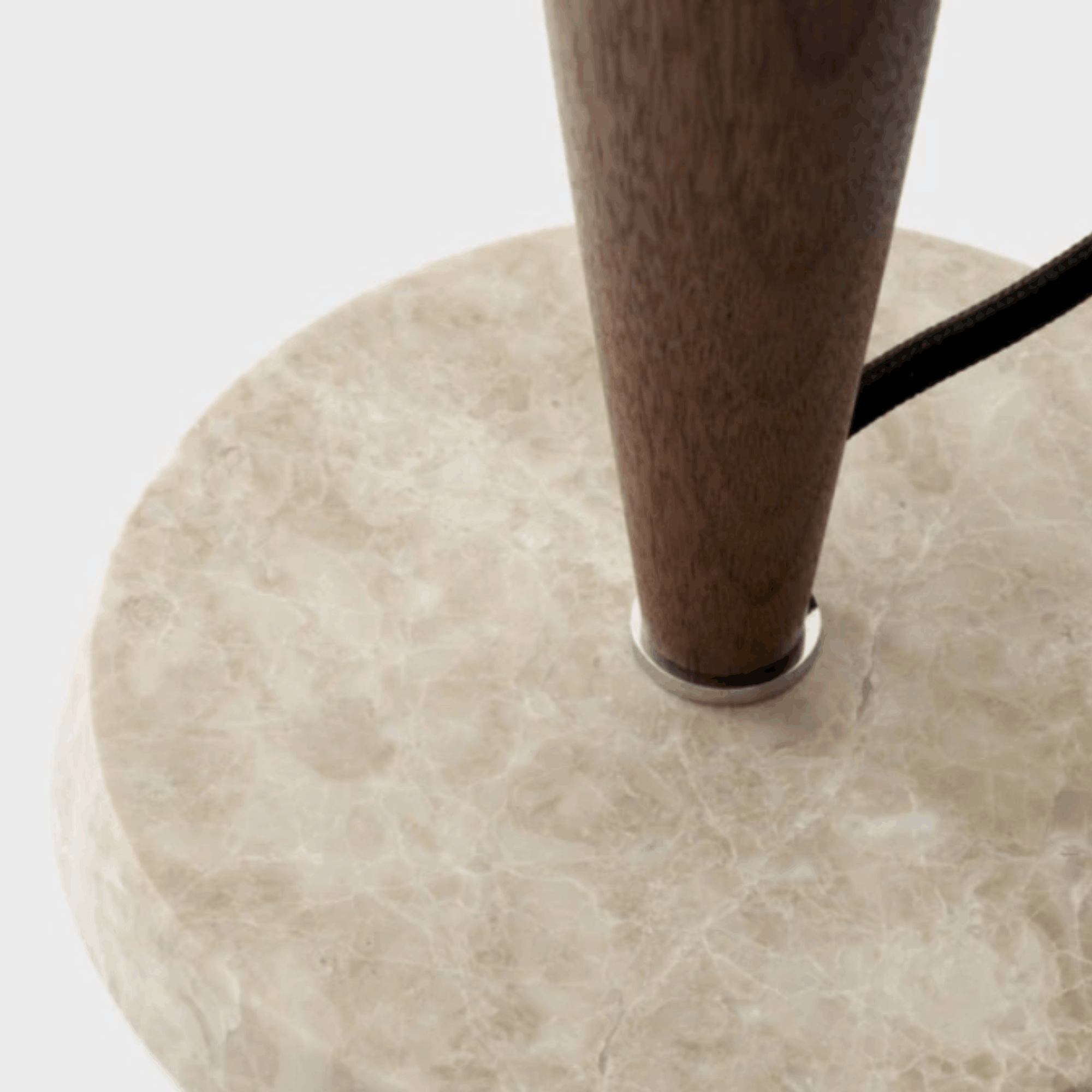 Close-up of a round light beige marble lamp base with a dark brown wooden leg and a black power cord, set against a plain white background.