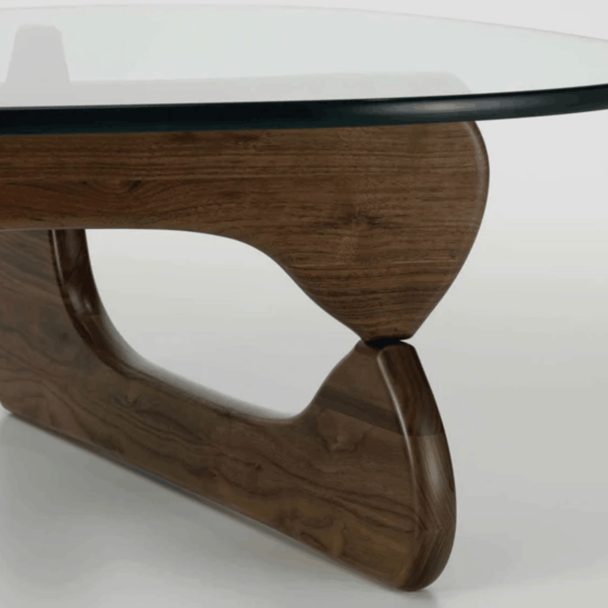 Close-up of a modern coffee table base with a curved, sculptural dark walnut wood design supporting a clear glass tabletop.
