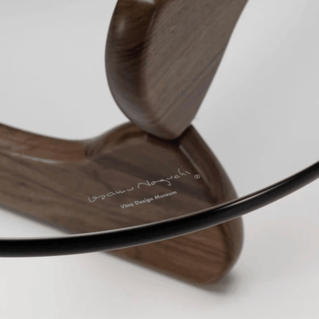 Close up of the Vitra Coffee Table by Isamu Noguchi in walnut with sculptural interlocking wooden base and curved clear glass top.